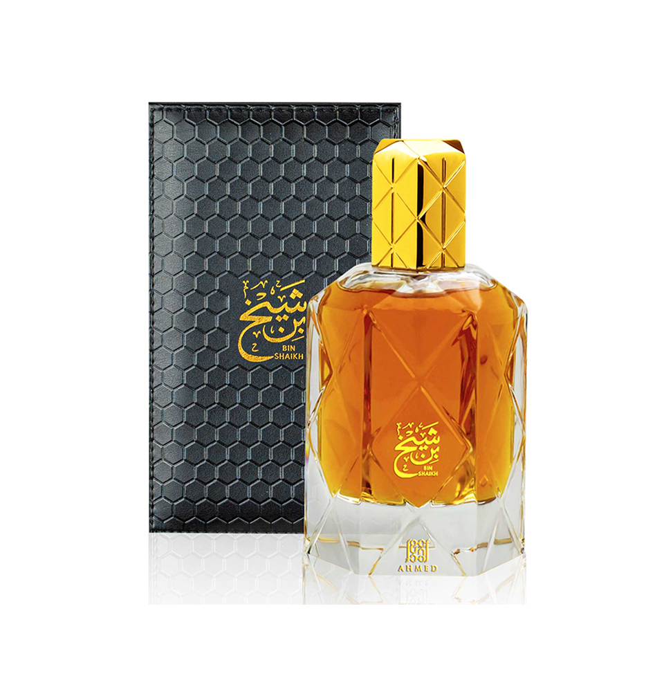 BIN SHAIKH BY AHMED AL MAGHRIBI EAU DE PARFUM 90ML FOR MEN & WOMEN: A clear, faceted bottle with golden liquid and gold details stands before a textured black box with matching gold accents, showcasing this elegant unisex fragrance.